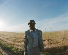 a man standing in the middle of a field with power lines behind him and sun shining on his face