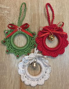 three crocheted christmas ornaments hanging on a wooden surface with bells attached to each ornament