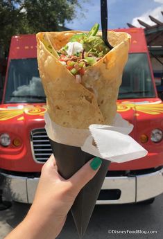 a person holding up a taco in front of a red truck