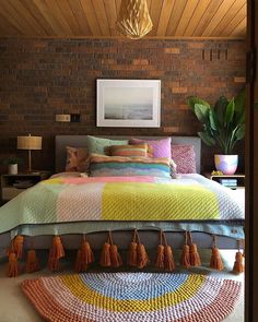 a bed with colorful blankets and tassels on the pillows is shown in front of a brick wall