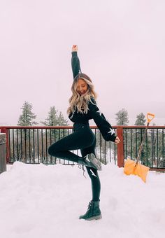 a woman standing in the snow with her arms up and legs crossed, holding an umbrella