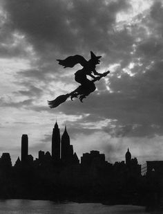 black and white photograph of two witches flying over the city