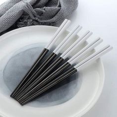 six black and white chopsticks are on a plate with a gray scarf in the background