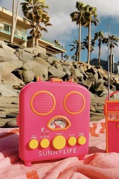 a pink radio sitting on top of a beach next to a red box and palm trees