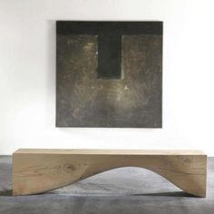 a wooden bench sitting in front of a painting on the wall with a black square above it