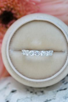 a diamond ring sits on top of a white velvet box with pink flowers in the background