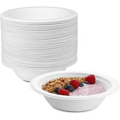 a white bowl filled with fruit and granola on top of a stack of plates