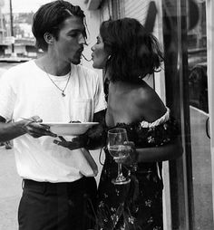 a man and woman kissing while holding a plate of food in front of a store