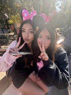 two girls with minnie ears on their heads posing for the camera and making peace signs