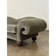 a grey velvet chaise lounge chair with wooden legs and foot rests on a wood floor