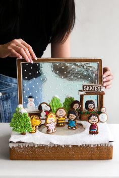 a woman holding up a fake snow scene in front of her face with other figurines