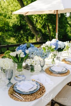 an outdoor table set with blue and white plates, napkins, and vases