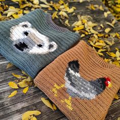 two knitted sweaters sitting on top of a wooden table covered in leaves and yellow leaves