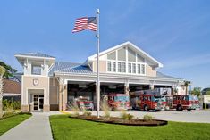 two fire trucks parked in front of a fire station with an american flag on top