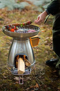 a man cooking food on top of a grill in the grass next to a forest