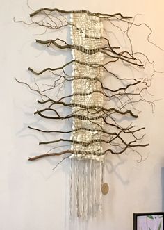 a piece of art made out of branches and beads hanging from the side of a wall