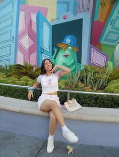 a woman is sitting on a wall talking on her cell phone and posing for the camera