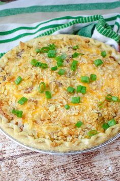 a pie sitting on top of a wooden table covered in cheese and green onion toppings