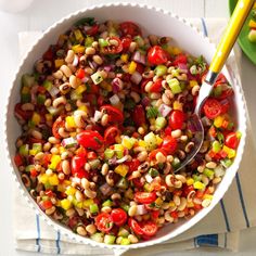 a white bowl filled with beans and veggies on top of a table next to a yellow spoon