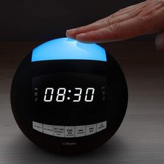 a person touching the time on an alarm clock that is lit up with blue light