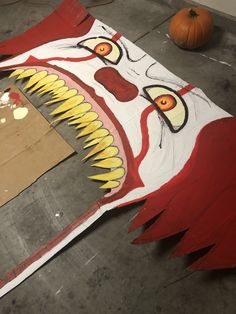 a painting of a clown's face on the floor next to a cardboard box