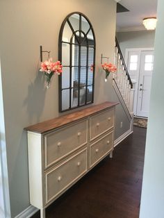 a dresser with flowers on it in front of a mirror and stairs leading up to the second floor