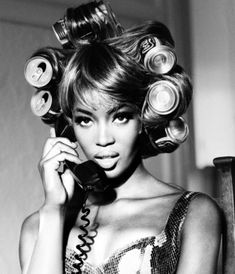 a black and white photo of a woman with curls on her head talking on the phone