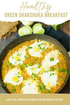 a pan filled with eggs and sauce on top of a wooden table next to bread