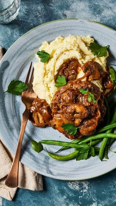 a plate with mashed potatoes, green beans and meat on it next to a fork