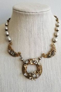 This is a vintage 1940s Original by Robert necklace. The necklace features a gold tone intricate metalwork with flowers and pearl tone details. The pearl tone beads are likely baroque style hand-painted glass given the era. The pearl tone beads range from brighter white to champagne to gray depending on the bead. The range of color could be intentional in design or from previous age and wear. The back of the center circle is signed on a palette shape. This necklace is in excellent condition.Cent Antique Baroque Jewelry For Wedding, Heirloom Baroque Jewelry For Weddings, Ornate Gold Necklaces For Vintage Events, Ornate Brass Necklaces For Wedding, Ornate Brass Necklace For Wedding, Ornate Antique Gold Necklace For Anniversary, Antique Gold Necklace With Antique Finish For Wedding, Antique Gold Wedding Necklace With Antique Finish, Ornate Gold Pearl Necklace For Wedding