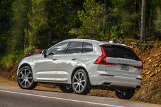 the rear end of a white volvo suv driving on a road in front of trees