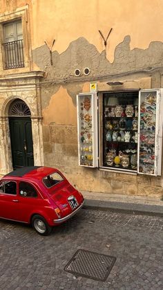 an old red car parked in front of a building with many items on the windows