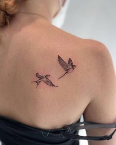 the back of a woman's shoulder with two small birds flying in opposite directions