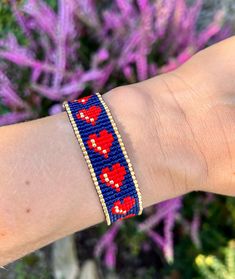 a woman's arm with a beaded bracelet on it and flowers in the background