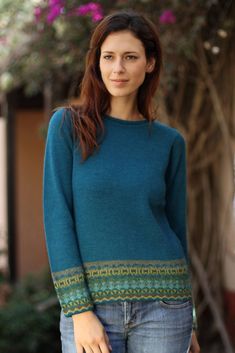 a woman standing in front of a tree with her hand on her hip wearing a blue sweater and jeans