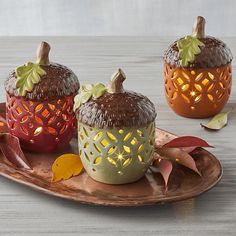 three decorative pumpkins sitting on top of a wooden platter with leaves and candles