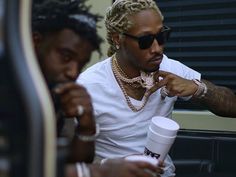 two men sitting next to each other holding coffee cups and looking at their cell phones