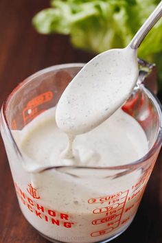 a measuring cup filled with dressing on top of a wooden table next to lettuce