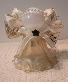 a glass bell with pearls and ribbon around it sitting on a white tableclothed surface