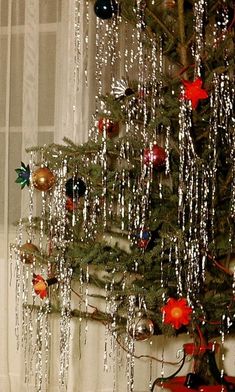 a small christmas tree with ornaments hanging from it's branches in front of a window