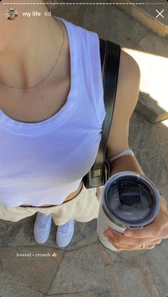 a woman holding a coffee cup and looking down at her cell phone while standing on the ground