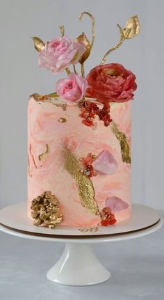 a pink cake with gold leaf and flowers on top