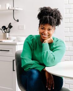 a woman sitting in a chair with her arms crossed and looking at the camera while smiling