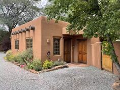 an adobe style house with flowers and trees in the front yard, surrounded by gravel