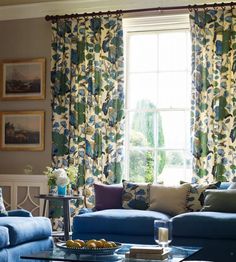 a living room filled with blue couches next to a window covered in floral curtains