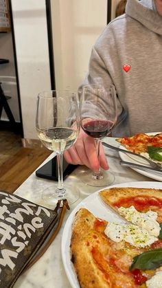 a man sitting at a table with two pizzas and glasses of wine in front of him