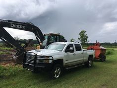 a white truck parked next to a bulldozer on top of a lush green field