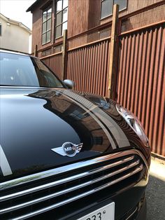 a black car is parked in front of a building with a brown fence behind it