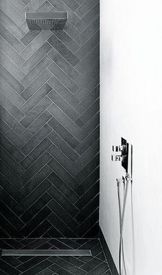 black and white photograph of a shower head in a bathroom with herringbone tile on the walls