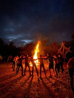 a group of people standing around a fire with their arms wrapped around each other in front of them